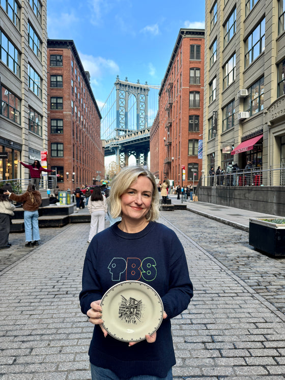 Person holding a plate in an urban setting with a bridge and buildings in the background