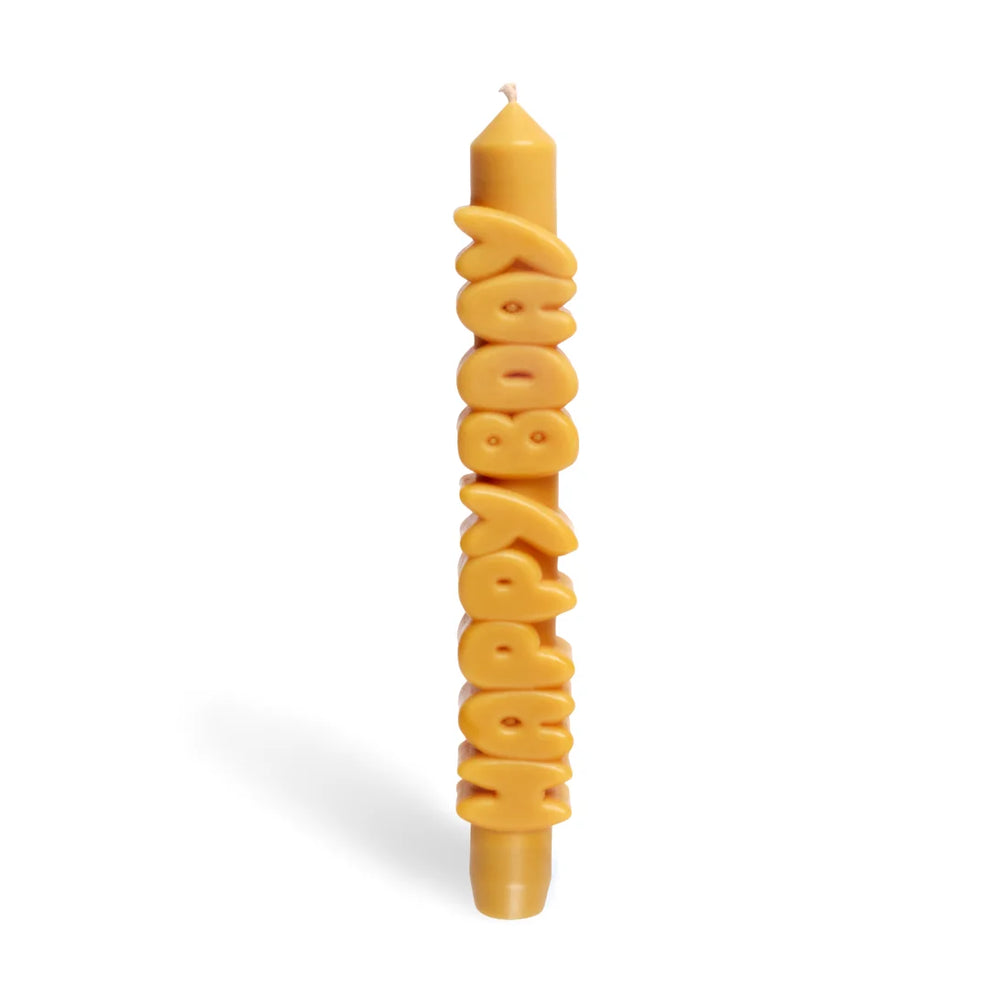 Mustard yellow taper candle with HAPPY BDAY spelled out in stacked sculpted letters