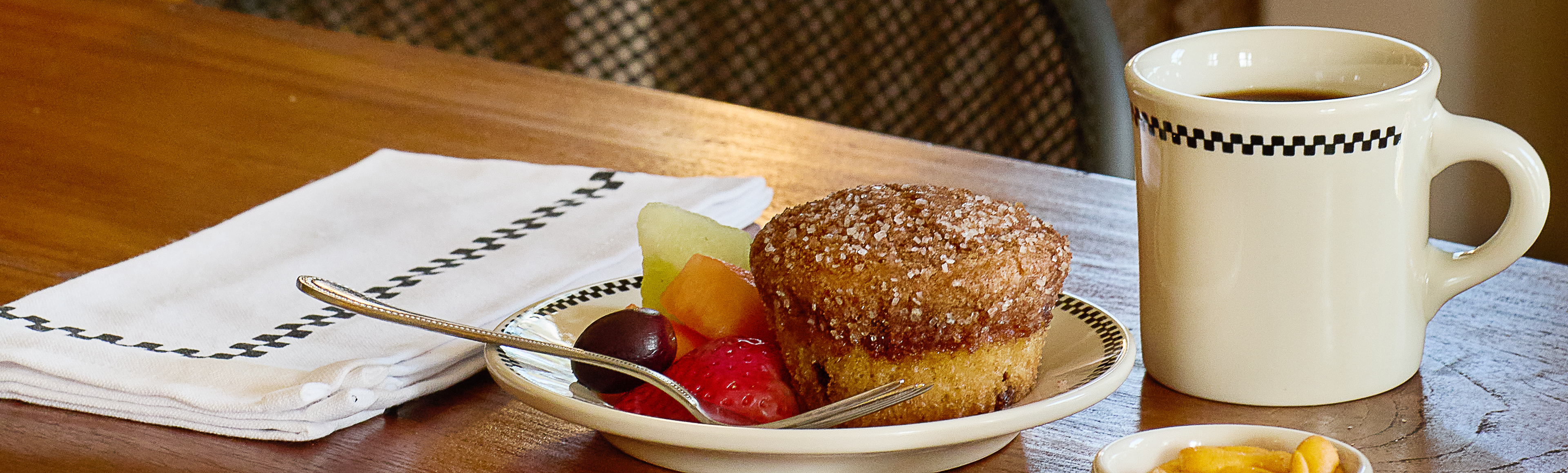 Muffin with fruit and chocolate on a plate next to a mug of coffee on a wooden table.