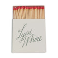 Square box of long red-tipped matches, open, white cover with Lyin' Whore in green cursive