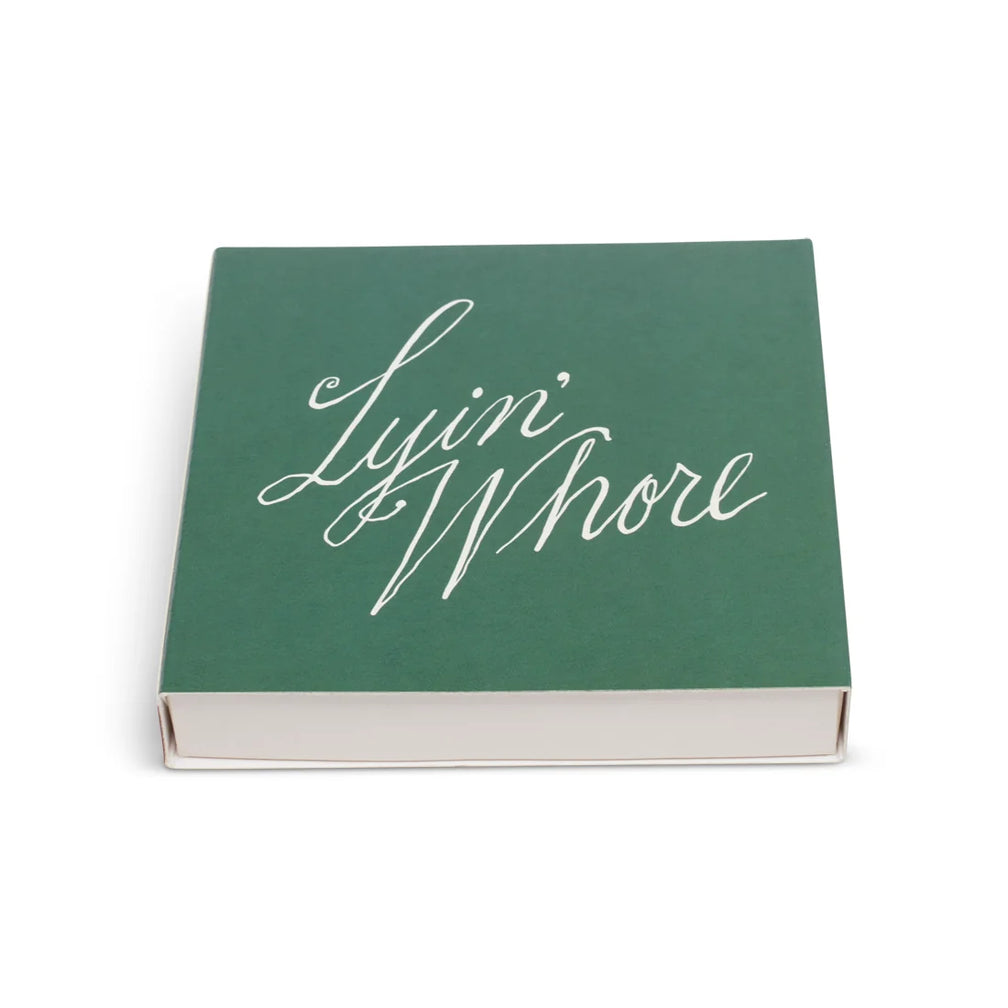 Green square matchbox with Lyin' Whore white cursive script, angled to show the side