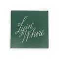 Green square matchbox cover, straight-on view of white cursive Lyin' Whore lettering