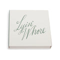 White square matchbox at an angle with Lyin' Whore in green cursive script
