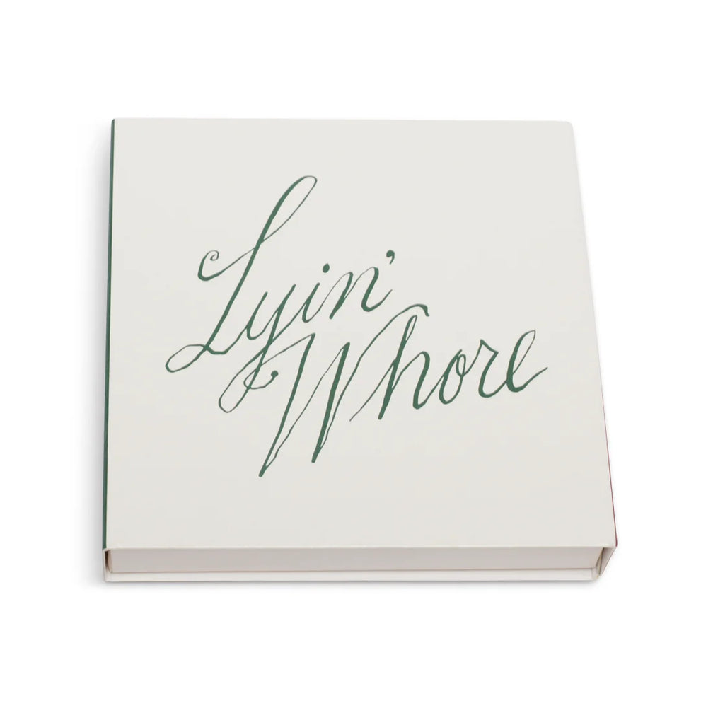 White square matchbox at an angle with Lyin' Whore in green cursive script