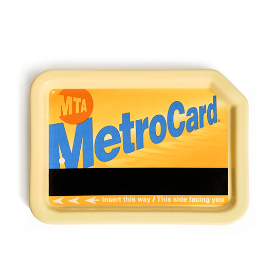 Yellow ceramic MetroCard tray styled like a classic MTA MetroCard, with warm yellow face, large blue MetroCard lettering, orange MTA logo, black magnetic stripe, and raised yellow rim; useful as a nostalgic NYC catchall for keys, coins, or jewelry, shown from above.