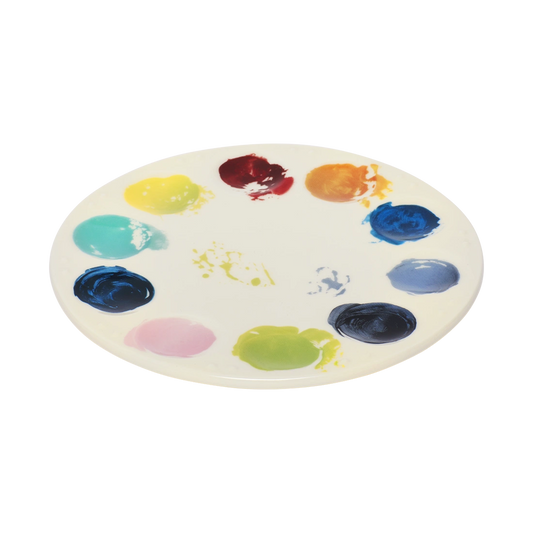 Artist palette ceramic plate with vibrant painted color swatches around the edge, designed to resemble a painter’s palette. Unique art-inspired serving plate for cheese boards, desserts, and creative table settings. Angled view.