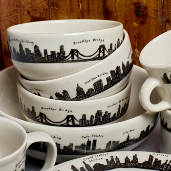 Set of ceramic bowls and mugs with city skyline designs on a wooden surface.