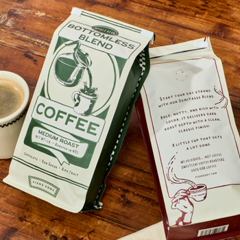 Two coffee packages labeled 'Bottomless Blend' on a wooden surface with a cup of coffee.