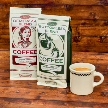 Two coffee bags labeled 'Demitasse Blend' and 'Bottomless Blend' on a wooden surface with a cup of coffee.