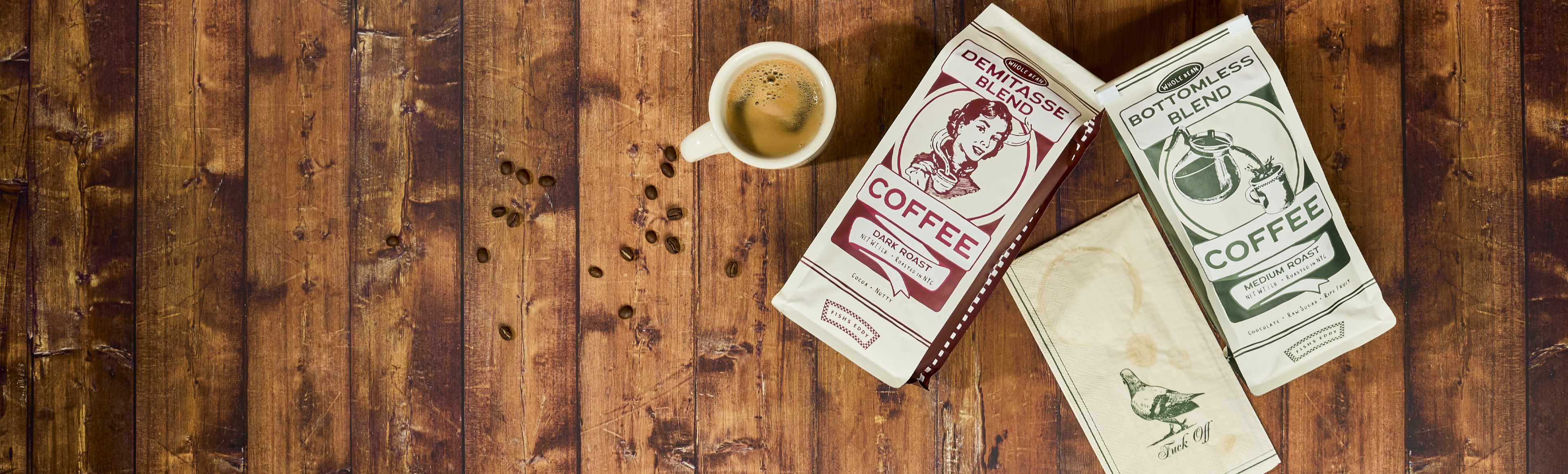 Three coffee packages and a cup of coffee on a wooden surface