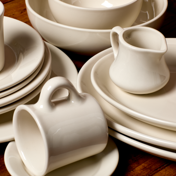 Set of white ceramic dishes including cups, saucers, and a pitcher on a wooden surface.