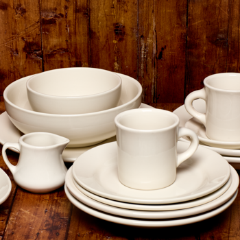 Set of white ceramic dishes including bowls, cups, and a pitcher on a wooden surface.