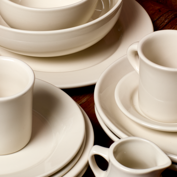 Set of white ceramic dishes including bowls, plates, and mugs on a wooden surface.