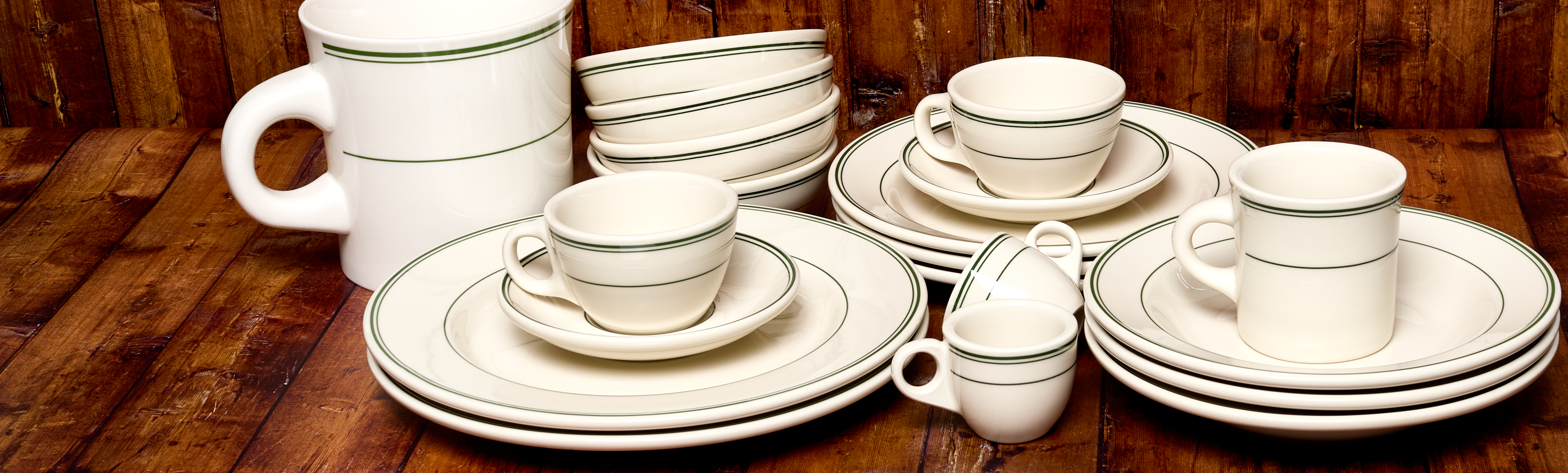 Set of white ceramic dinnerware with green trim on a wooden surface