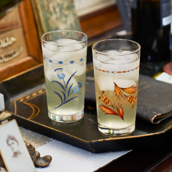 Two glasses with decorative designs on a tray with a bottle in the background
