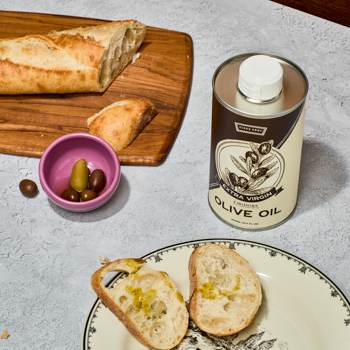 Olive oil can with bread slices and olives on a plate and cutting board.