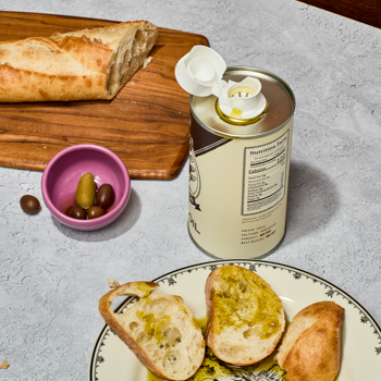 Can of olive oil with bread and olives on a table