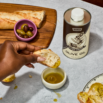 Person dipping bread into olive oil with a can of olive oil in the background
