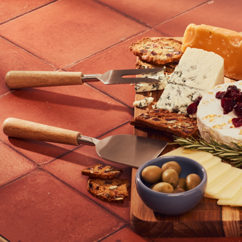 Cheese platter with crackers, olives, and cheese knives on a terracotta surface.