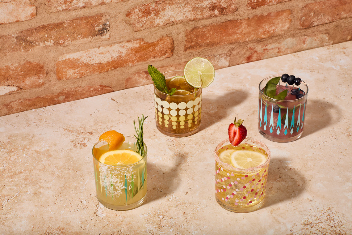 Four cocktails in decorative glasses on a stone surface with a brick wall background