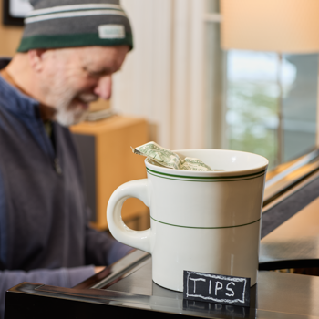 Person sitting at a table with a large mug labeled 'TIPS' and a small bag of money inside.