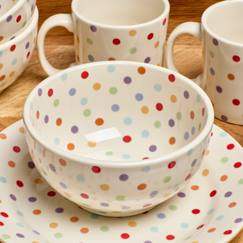 Polka dot ceramic bowl, mug, and plate on a wooden surface