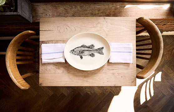 Wooden table setting with a plate featuring a fish illustration, surrounded by chairs.