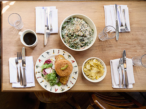 Dining table set with a meal including salad, bread, and pasta, accompanied by cutlery and glasses.