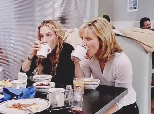 Two women sitting at a table in a cafe, drinking coffee and eating.