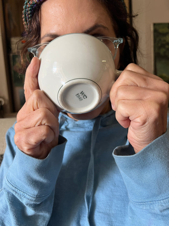Person holding a white mug with a brand logo, wearing a blue shirt.