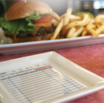 Tray with a checkered pattern and text, blurred background of a burger and fries.