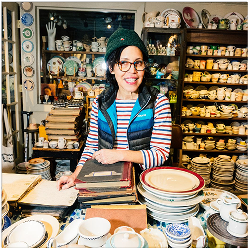 Person in a antique store surrounded by books and ceramic items.